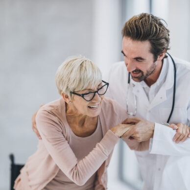 Shot of a young doctor helping a senior woman in a wheelchair at the hospital hallway.